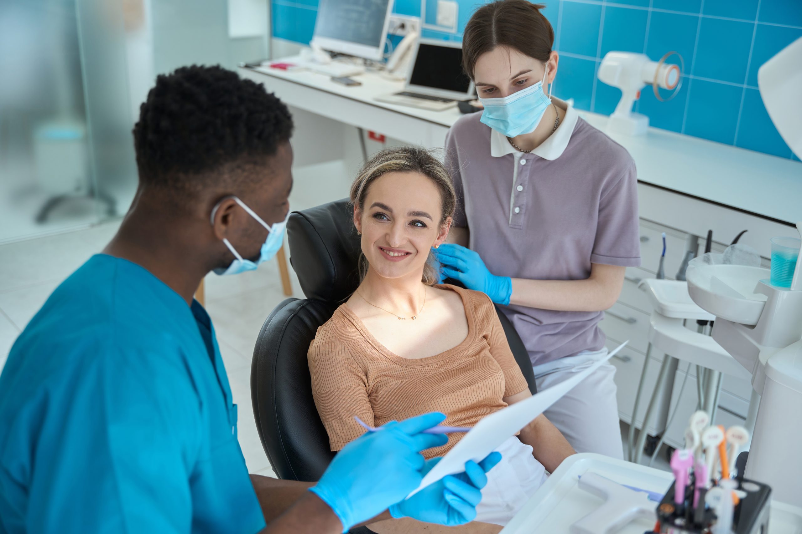 Young man in protective gloves and blue suit sitting near patient and showing x ray in the clinic
